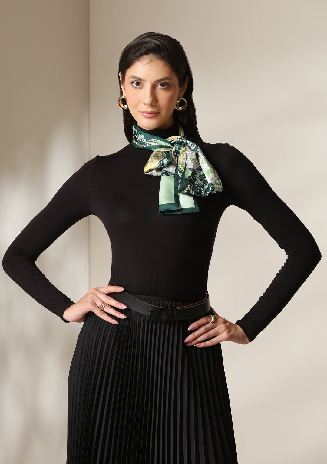 Woman wearing a botanical paisley silk scarf styled over a black turtleneck and pleated skirt