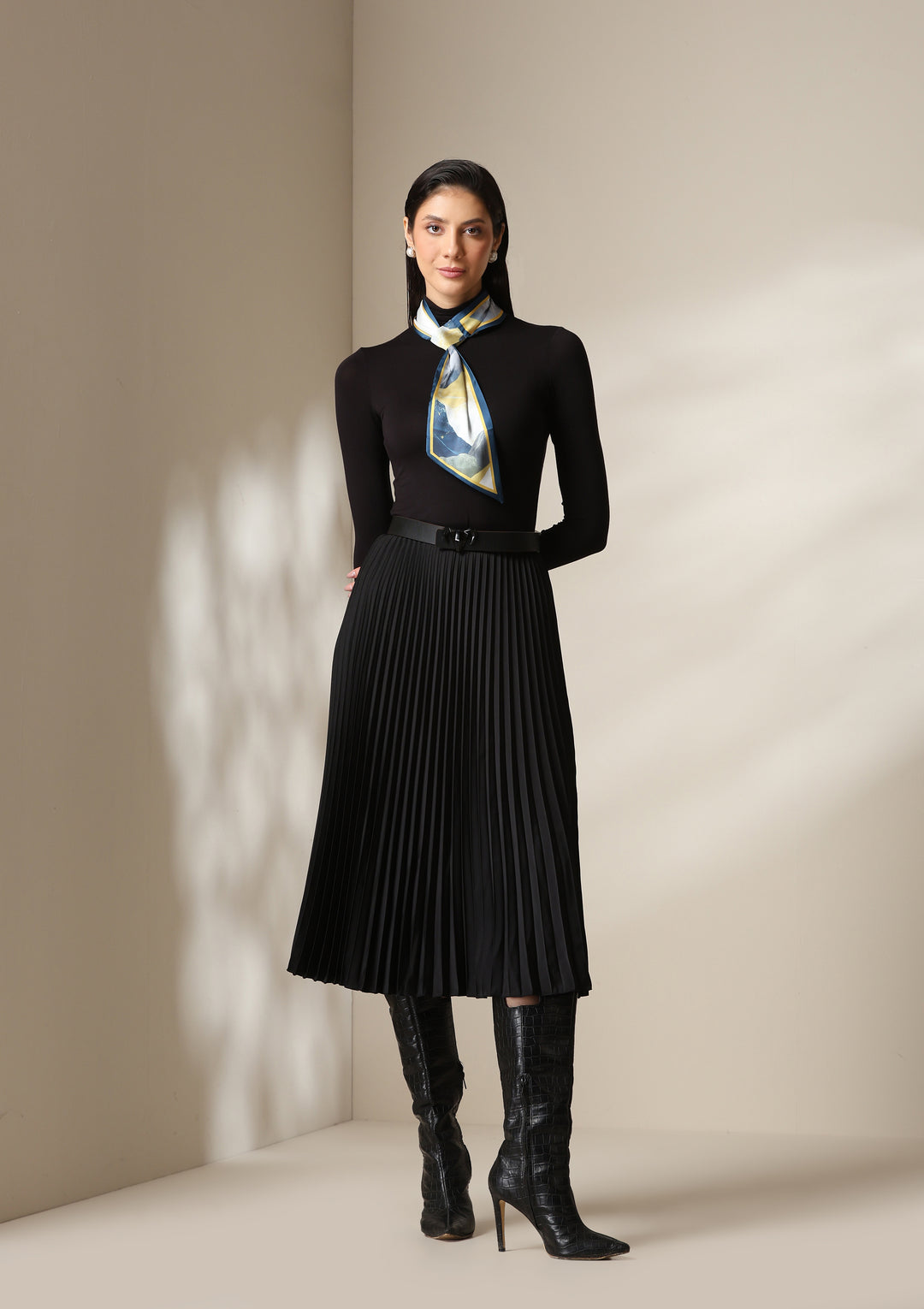 Woman wearing a multicolour abstract silk scarf styled around the neck with a black turtleneck and pleated skirt