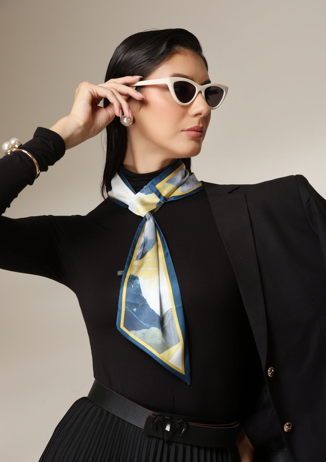 Woman wearing a multicolour abstract silk scarf styled around the neck with a black turtleneck and pleated skirt