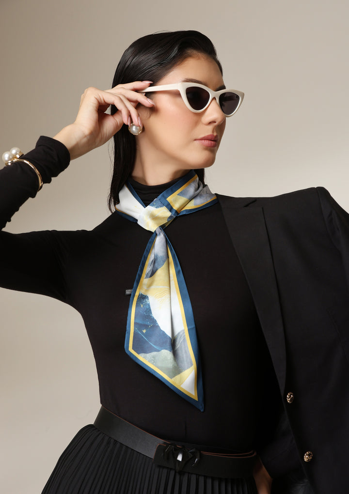 Woman wearing a multicolour abstract silk scarf styled around the neck with a black turtleneck and pleated skirt