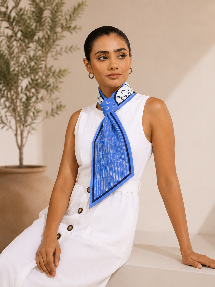 Woman wearing a blue silk neck scarf with ivory print and navy border styled with a white sleeveless top